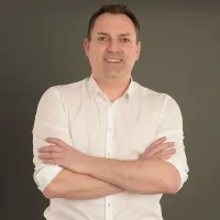 Porträt von Ralf Dodler in weißem Hemd vor dunklem Hintergrund.