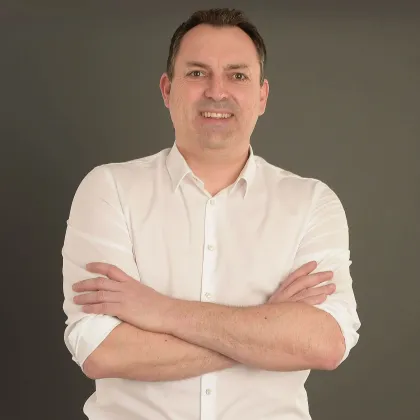 Porträt von Ralf Dodler in weißem Hemd vor dunklem Hintergrund.