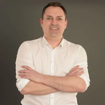 Ralf Dodler im weißen Hemd vor braunem Hintergrund